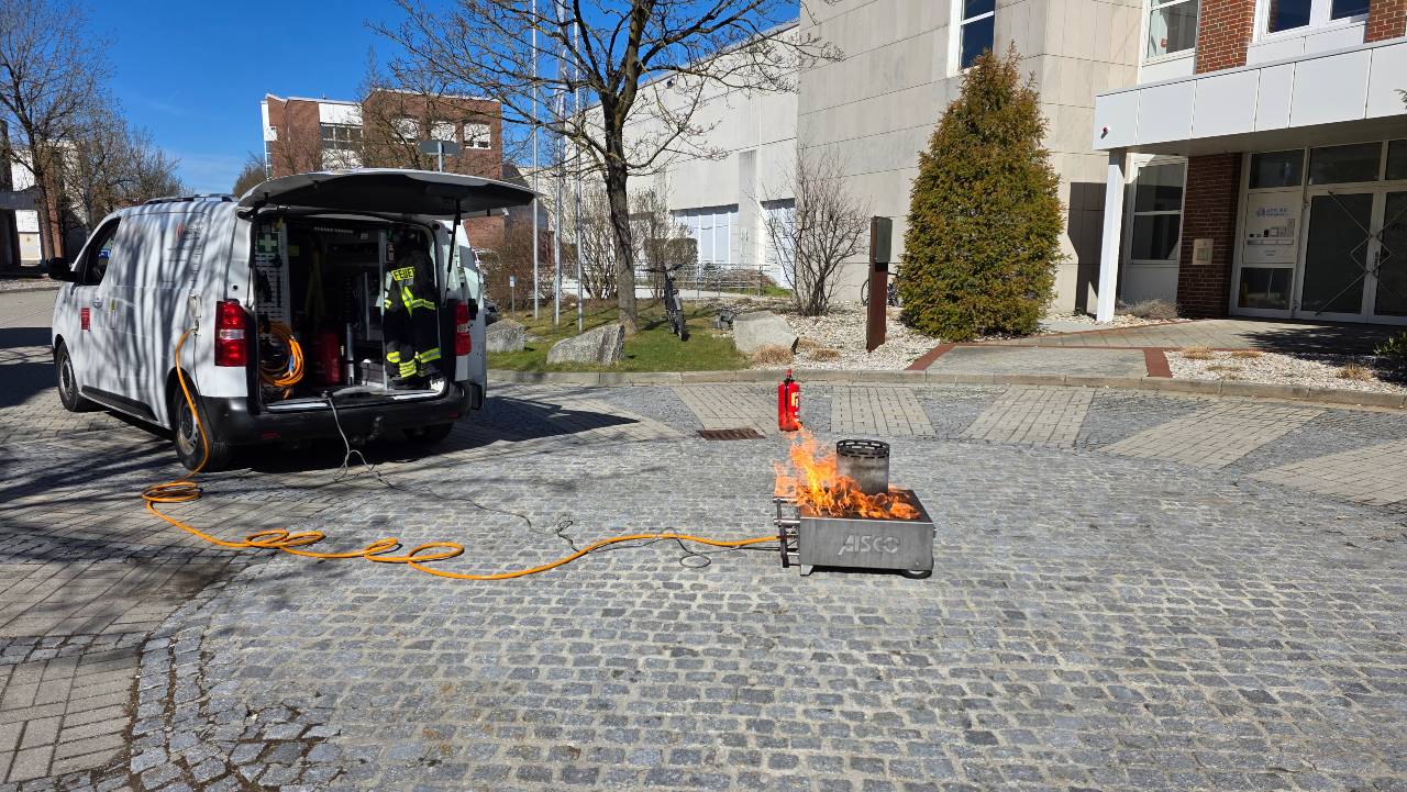Feuerlöscher-Training im Freien mit Servicefahrzeug, Ausrüstung, kontrollierte Flamme in Übungsschale und Feuerlöscher vor Gebäude